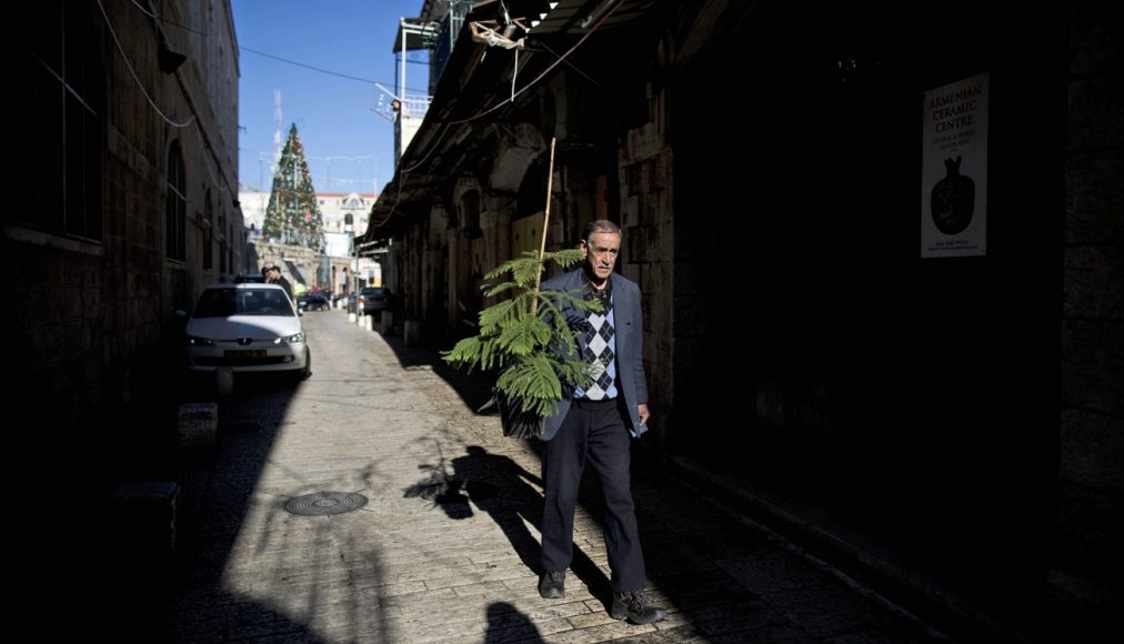 Un Palestinien portant un sapin de Noël dans une rue pavée de la vieille-ville de Jérusalem. / Keystone/ Abir Sultan